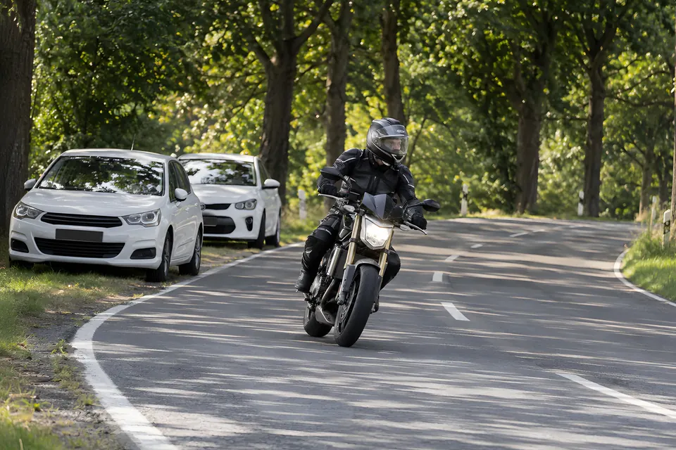 Motorradfahrer in Schutzkleidung in einer Kurve auf einer Allee