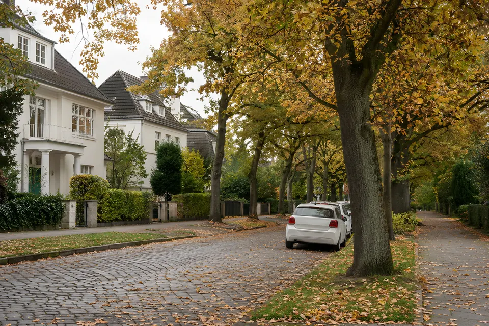 Stimmungsbild: Kopfsteinpflasterstraße unter Herbstbäumen mit weißen Häusern und einem geparkten Auto