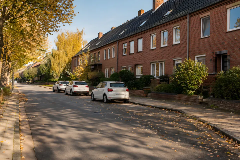 Stimmungsbild: Wohnstraße mit Backsteinhäusern, Bäumen und geparkten Autos im Herbstlicht