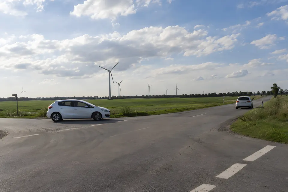 Stimmungsbild: Straßeneinmündung am Feldrand mit zwei weißen Autos und Windrädern am Horizont