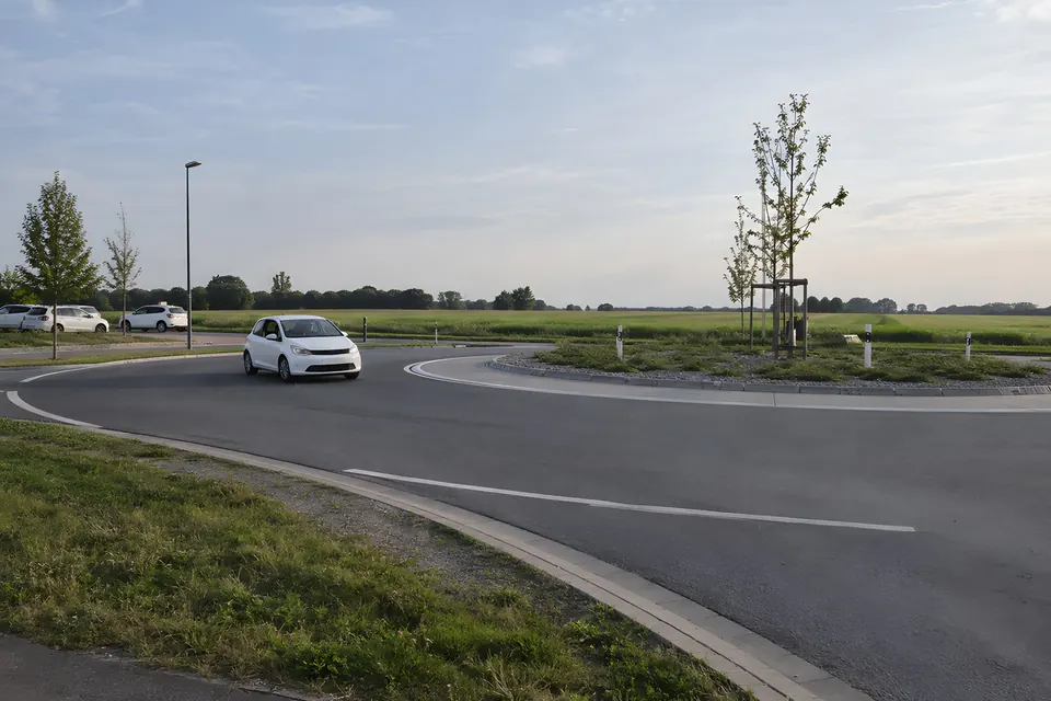 Stimmungsbild: Kreisverkehr am Ortsrand mit einem weißen Auto und weiten Feldern im Hintergrund