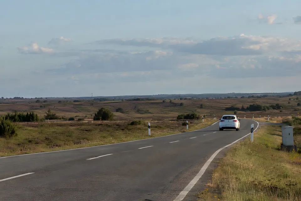 Stimmungsbild: Landstraße durch eine weite Heidelandschaft mit einem weißen Auto